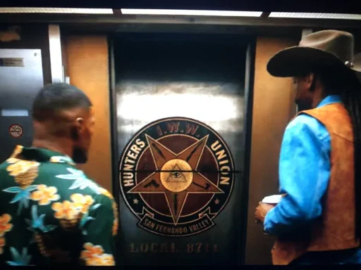 Screenshot from "Day Shift" (2022) weather to protagonists are standing in front of an elevator as it opens. the elevator door has a logo emblazoned on it, of the iww hunters Union San Fernando valley, local 8714 branch. the logo has a pyramid with an eye in the center, like the Illuminati logo, and an upside down red star with each point of the Stark containing weapons such as a handgun, shotgun, and knives.